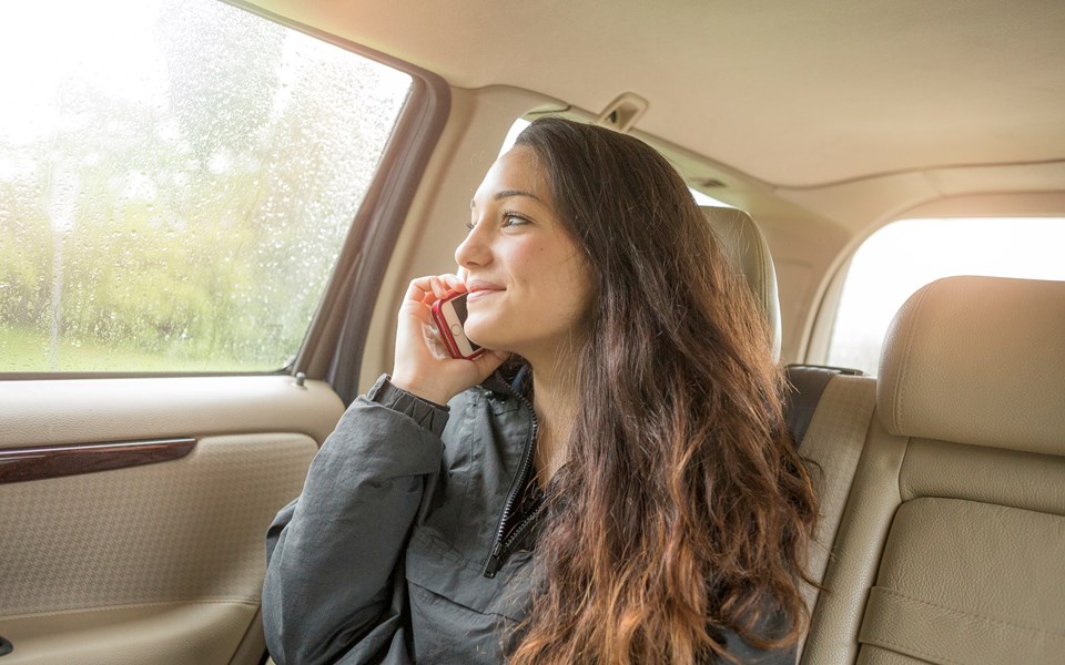 En ung kvinna sitter i baksätet på en bil och talar i mobiltelefon medan hon tittar ut.