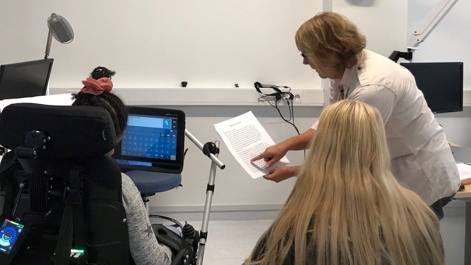 Kvinna läser text för elev. Elev arbetar på datorskärm framför sig.